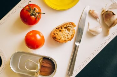 Tomatoes, bread, and sardines arranged for Catalán toast preparation.